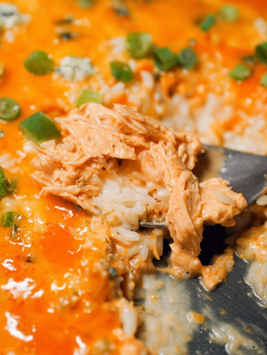 Łyżka zanurzona w kremowym daniu z kurczaka i ryżu z sosem buffalo.