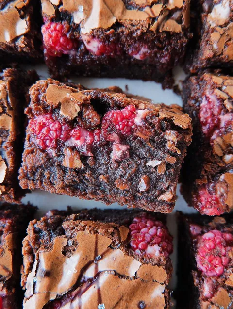 Zbliżenie czekoladowego brownie z malinami na wierzchu.