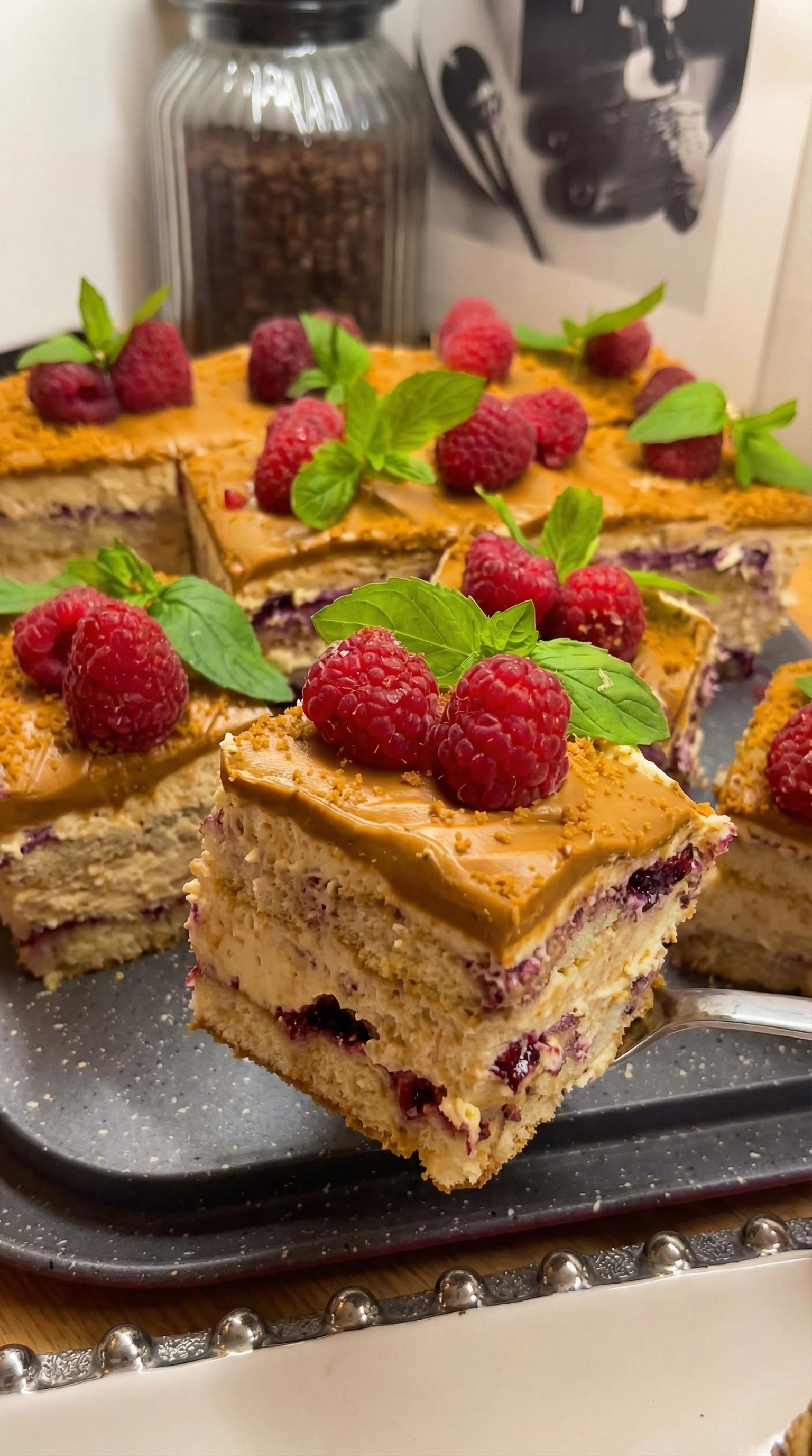 A slice of tiramisu lotus cake with raspberries on top.