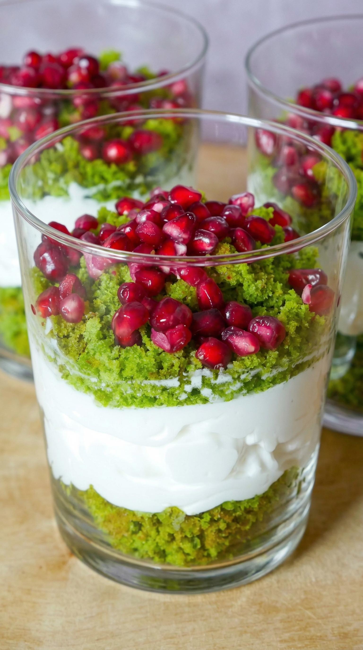 A glass of food with pomegranate seeds and white cream.