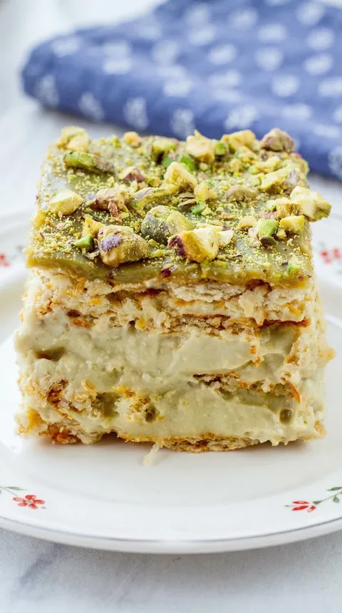 A slice of cake with pistachio nuts on top.