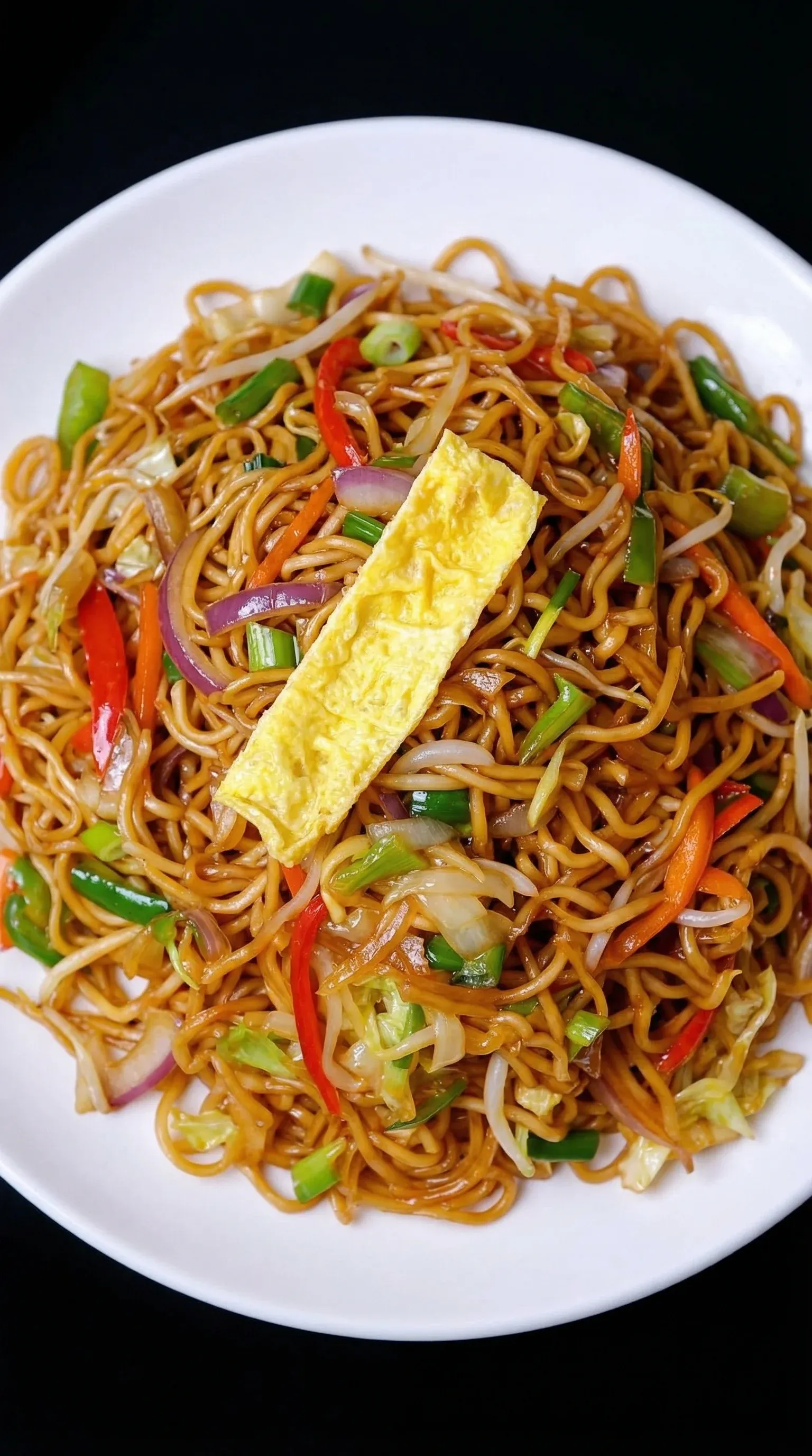 A plate of noodles with vegetables and a fried egg on top.