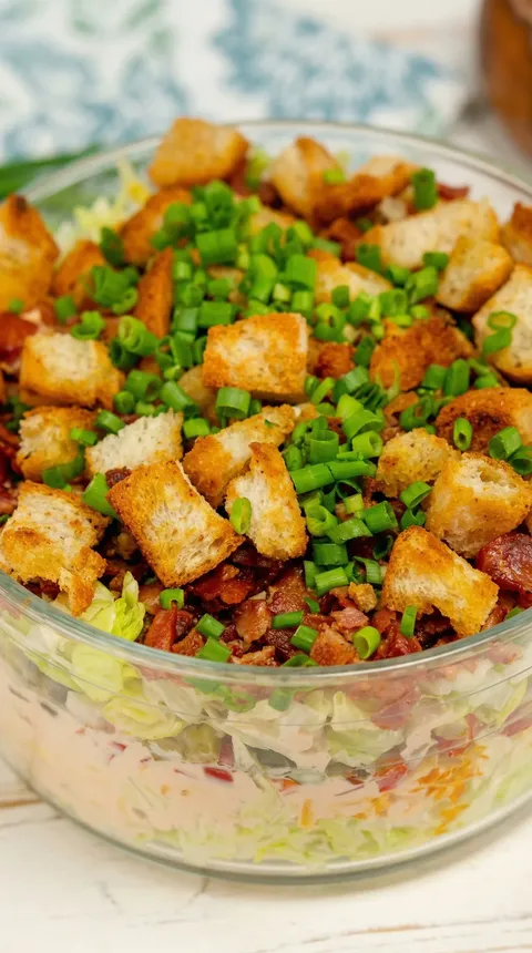 A bowl of salad with toast and bacon.