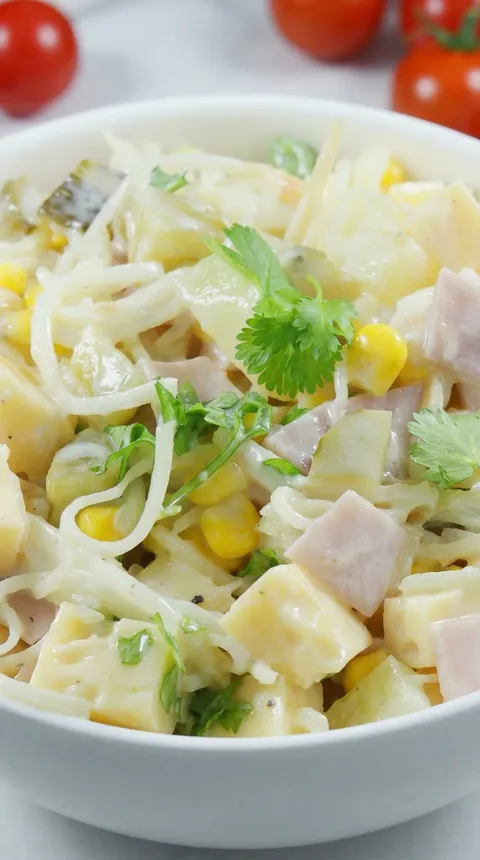 A close up of a salad with noodles, corn, and ham.