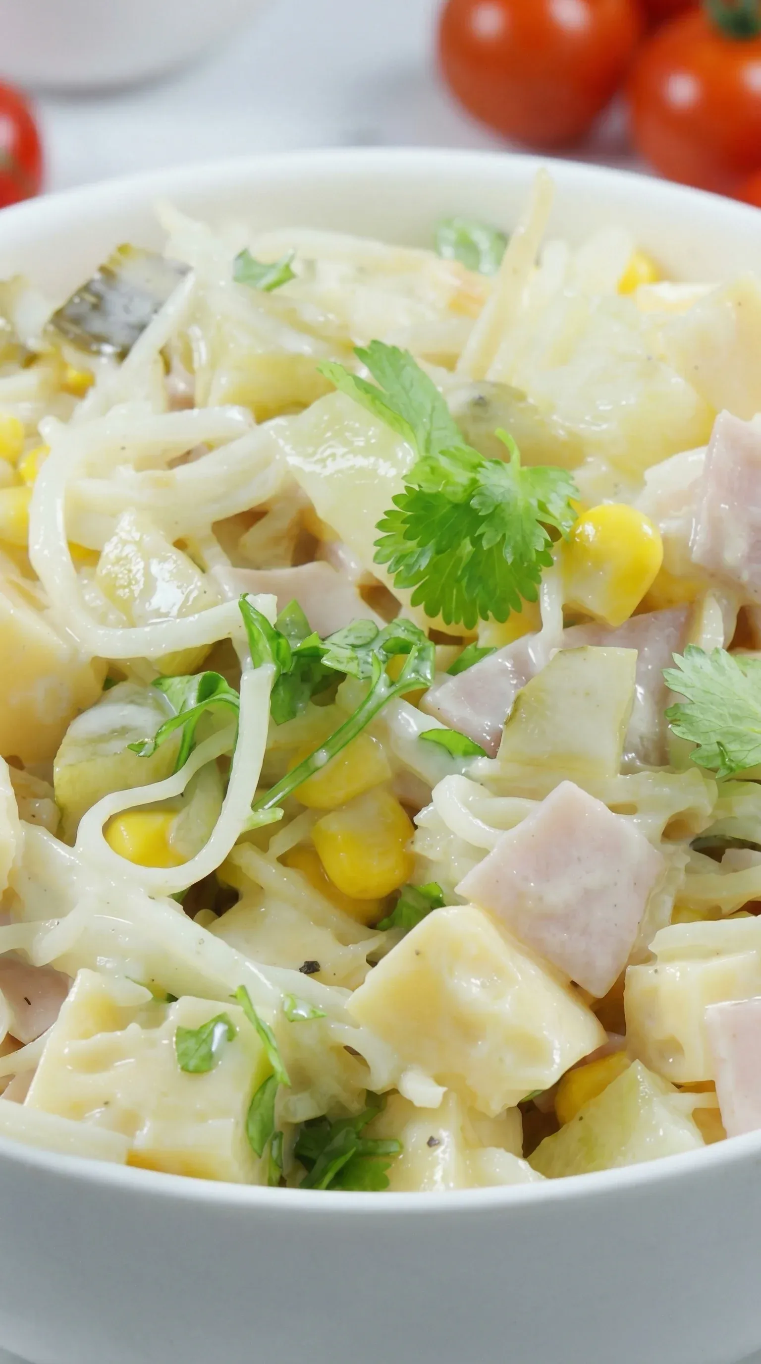 A bowl of food with noodles, corn, and ham.