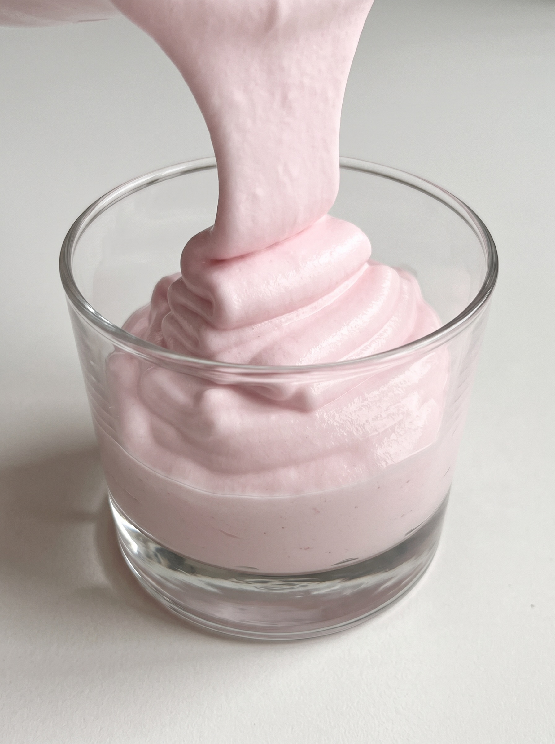 A glass of pink cream with a spoon in it.