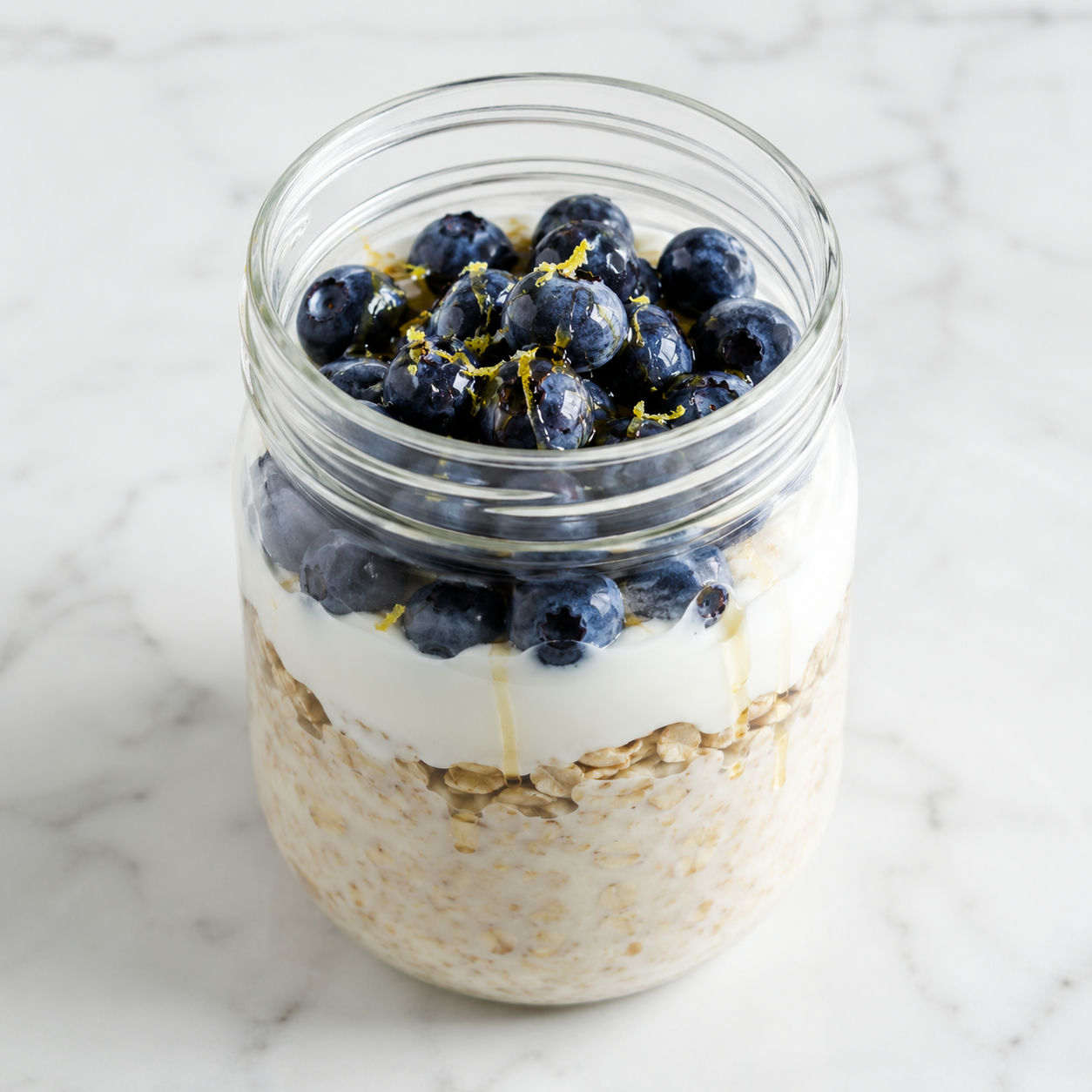 Blueberry overnight oats in a glass jar with honey and lemon zest