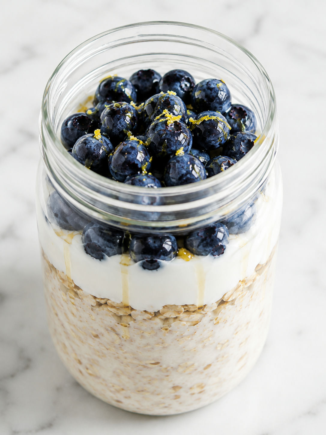 Blueberry overnight oats filling a glass jar with honey and fresh berries